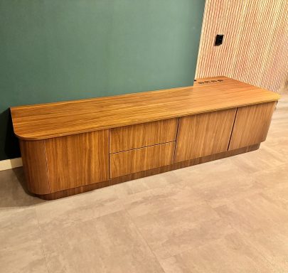 Lage houten kast met schuifdeuren tegen een groene muur.