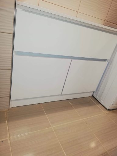 Witte kastdeuren onder een aanrecht, met een lichte tegelvloer eromheen.