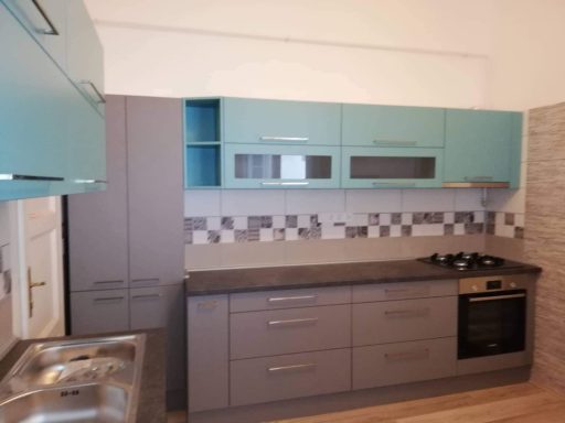 Moderne keuken met turquoise en grijze kasten, gasfornuis en tegelachtergrond.