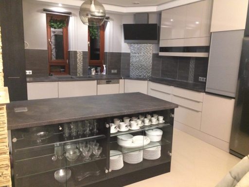 Moderne keuken met eiland, grijze kasten en glazen servies.