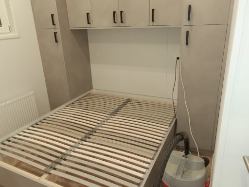Minimalistische slaapkamer met een bed waarop latten, zonder matras en met een stofzuiger erbij.