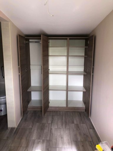 Lege kast met open deuren en planken, tegen een lichte muur.