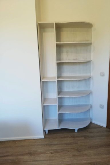 Witte, ronde boekenkast met meerdere planken tegen een muur.