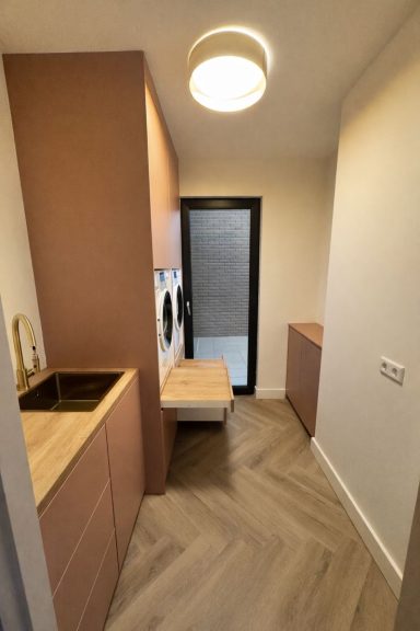 Moderne keuken met houten accenten, wasmachine en toegang tot buiten.