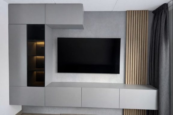 Moderne woonkamer met een strakke grijze wandmeubel en een televisiescherm.
