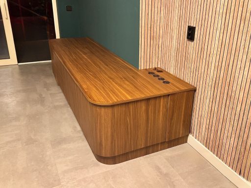 Lange houten meubel met een afgeronde voorkant en aansluitpunten aan de bovenkant.