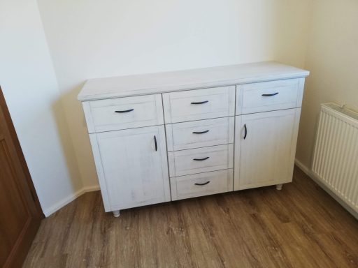 Witte kast met zes lades en een open bovenstuk, geplaatst in een lichte kamer.
