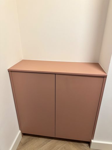 Roze kast met twee deuren, geplaatst in een hoek van een kamer.